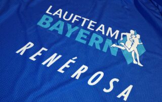 Die Logos von Laufteam Bayern und unserem Exklusivausrüster RenéRosa auf einem Raceshirt.